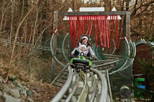 mor med dotter rida elektrisk släde på skenor. foto