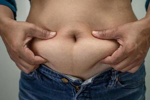 överviktig asiatisk kvinna visar fet mage på kontoret. foto