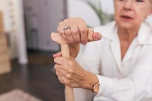 händer av ett gammal kvinna med en sockerrör, äldre lady Sammanträde på de soffa med trä- gående pinne. beskurna skott av en senior kvinna innehav en sockerrör i en pensionering Hem foto