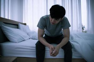 betonade asiatisk ung man Sammanträde ensam på säng. dålig relation eller bankrutt problem och sjukdom begrepp. foto
