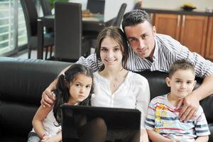 Lycklig ung familj ha roligt och arbetssätt på bärbar dator på Hem foto