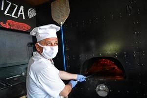 kock med skyddande coronavirus ansikte mask framställning pizza foto