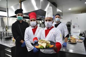 grupp kockar stående tillsammans i de kök på restaurang bär skyddande medicinsk mask och handskar i coronavirus ny vanligt begrepp foto