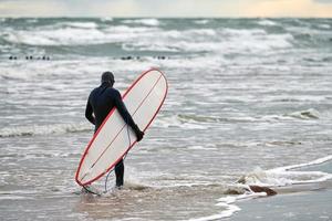 manlig surfare i baddräkt som går längs havet med surfbräda foto