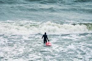 manlig surfare i baddräkt i havet med röd surfbräda foto