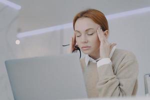 sjuk ung kvinna har tinningar smärta på kontoret. anställd har huvudvärk på arbetsplatsen. foto