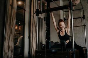 ung atletisk kvinna stretching kropp på pilates cadillac reformator foto