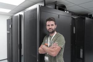 porträtt av manlig tekniker eller nätverk administratör stående modig som en hjälte med vapen korsade i data Centrum server rum. foto