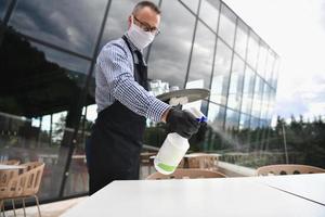 servitör rengöring de tabell med desinfektionsmedel spray i en restaurang foto