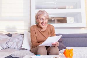 senior kvinna smilling och Lycklig handla om henne finanser. gammal lady mottar en brev.senior lady tar emot Bra Nyheter från en papper post. foto