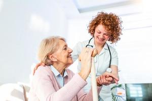 Lycklig patient är innehav vårdgivare för en hand medan utgifterna tid tillsammans. äldre kvinna i amning Hem och sjuksköterska. åldrig elegant kvinna på amning Hem foto