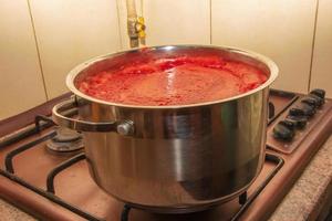 en kvinna förbereder färsk friska juice från tomater. nyligen tillverkad tomat juice är kokt i en kastrull och bevarad för långsiktigt lagring. diet begrepp för en friska livsstil. foto