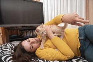 skön ung latinamerikan kvinna liggande på henne säng kramas och spelar med henne liten ljus brun katt foto