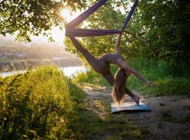 en ung gymnast är engagerad i antenn yoga i natur i de parkera, använder sig av en kombination av traditionell yoga poserar, pilates och mild dansa foto