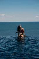 Lycklig kvinna i baddräkt simning i oändlighet slå samman mot vid havet. foto