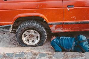 man lögner under en 4x4 bil på en smuts väg foto