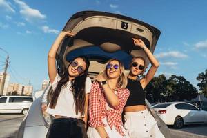 tre ung kvinna Framställ för de kamera de bil parkera. foto