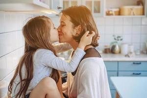 mamma kyssar henne liten dotter i de kök foto