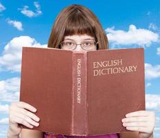 flicka utseende över engelsk ordbok och blå himmel foto