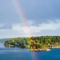 grön ö med by och regnbåge i blå himmel foto