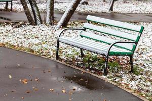 de först snö på trä- bänk i stad parkera foto