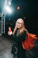 blond kvinna med smartphone på natt i de gata. foto