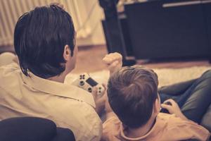 bak- se av far och son fira seger medan spelar video spel på Hem. foto