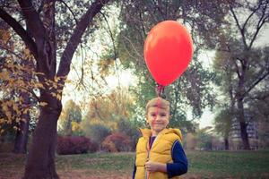 Lycklig unge med röd ballong i de parkera. foto