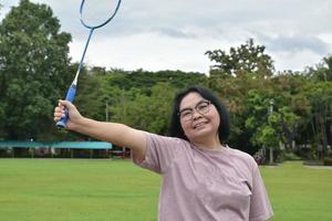 utomhus- badminton spelar, mjuk och selektiv fokus på vit fjäderboll, suddig asiatisk kvinna och träd bakgrund, begrepp för utomhus- badminton spelar i lediga tider och dagligen aktivitet. foto