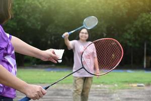 utomhus- badminton spelar, mjuk och selektiv fokus på vit fjäderboll, suddig asiatisk kvinna och träd bakgrund, begrepp för utomhus- badminton spelar i lediga tider och dagligen aktivitet. foto