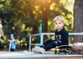 ung unge Sammanträde i de parkera på en skateboard. foto