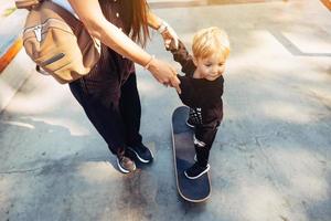 ung mor lär henne liten pojke till rida en skateboard foto