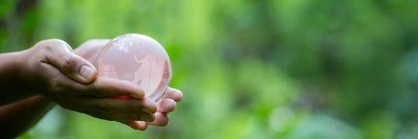 mänsklig hand innehav klot planet glas i grön skog med bokeh natur lampor. värld miljö dag. baner för miljö bevarande, skydda ekologi jord och miljö- miljövänlig liv. foto