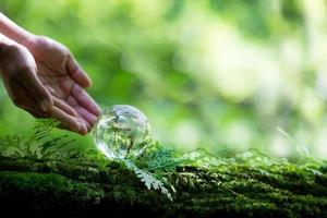 mänsklig hand innehav klot planet glas i grön skog med bokeh natur lampor. värld miljö dag. begrepp för miljö bevarande, skydda ekologi jord och miljö- miljövänlig liv. foto