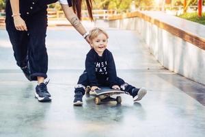 ung mor lär henne liten pojke till rida en skateboard foto