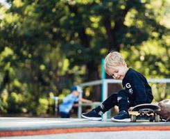 ung unge Sammanträde i de parkera på en skateboard. foto