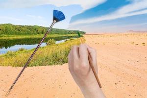 hand med paintbrush målarfärger flod i sand öken- foto