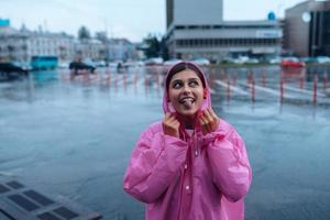 ung leende kvinna i en rosa regnkappa njuter en regnig dag. foto