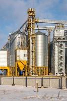 agro silos spannmålsmagasin hiss i vinterdag i snöiga fält. silos på en produktionsanläggning för jordbruksbearbetning för bearbetning av kemtvätt och lagring av jordbruksprodukter, mjöl, spannmål och spannmål. foto
