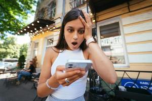 Söt kvinna ett urban gata till läsa ett SMS på henne mobil telefon foto