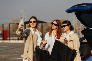 ung kvinnor på de bil med handla påsar. flickor ta selfie foto