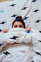 närbild av härlig ung kvinna lögner i säng täckt med filt. foto