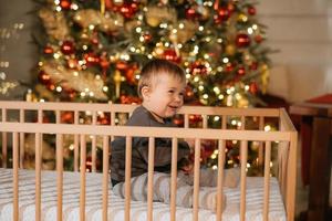 söt liten bebis på en spjälsäng förbi en jul träd, stänga upp foto