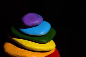 flera ljust färgad småsten målad i regnbåge färger lögn på topp av ett annan i främre av en mörk bakgrund foto