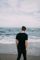 leende kille i en svart t-shirt står på de sandig stranden. foto