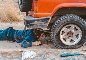 man lögner under en 4x4 bil på en smuts väg foto