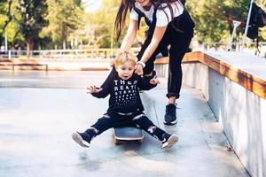 ung mor lär henne liten pojke till rida en skateboard foto