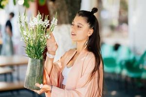 kvinna håll en vas av blommor i de gata Kafé foto