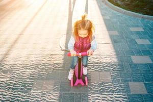 liten flicka med blond hår rider på skoter foto