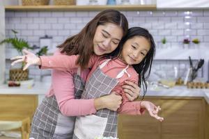 Lycklig asiatisk mor är kramas henne dotter medan har roligt tid efter matlagning i de kök för kärlek och familj begrepp foto